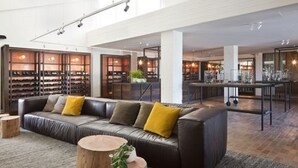 Un vaste espace salon avec un canapé en cuir, des tables rondes en bois et un meuble à vin en arrière-plan.