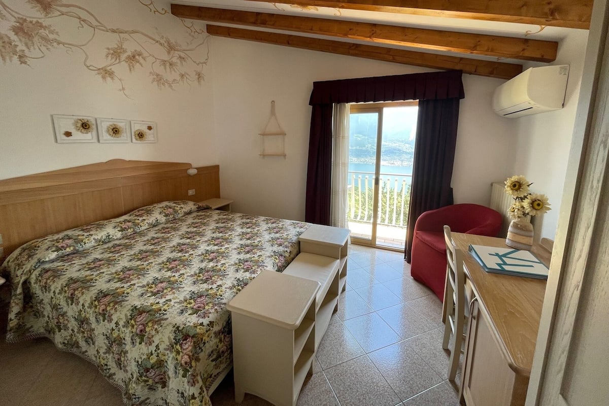 Een slaapkamer met een bed, bureau, stoel, raam met uitzicht en een houten plafond.