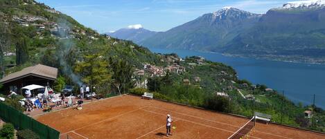 Ein Tennisplatz mit Netz, umgeben von Grün und einer Bergkulisse.