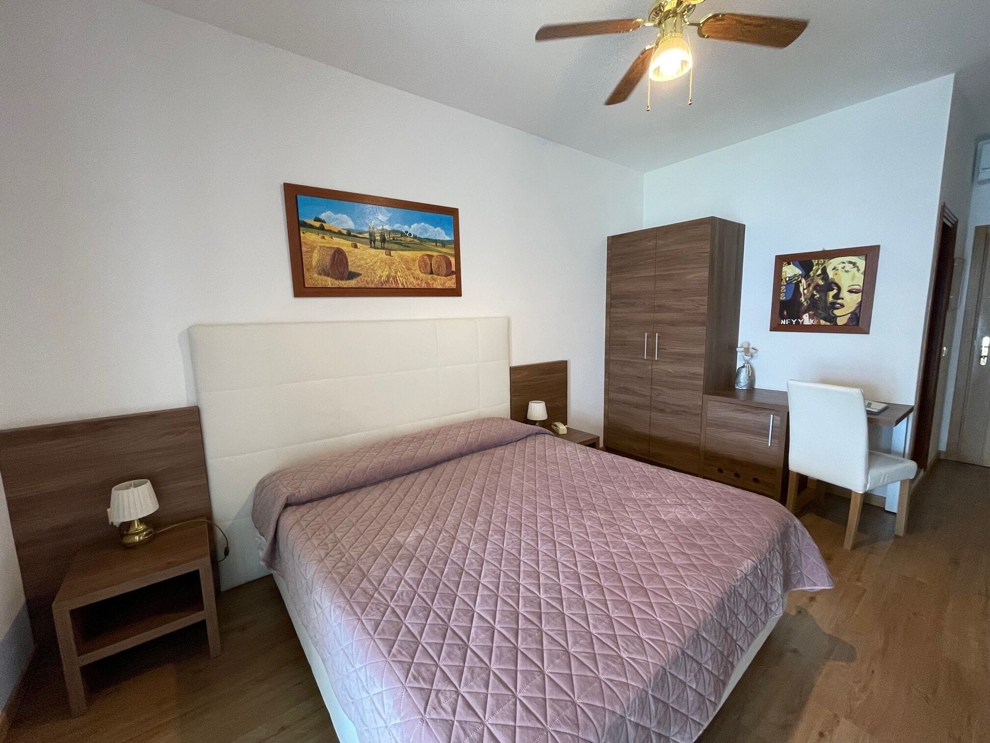 Un dormitorio con cama, mesitas de noche, armario, escritorio y ventilador de techo.