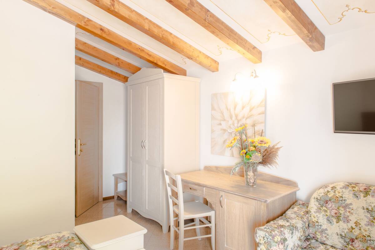 Een kamer met een houten plafond, een witte kast, een bureau met stoel en een bloemenbank.