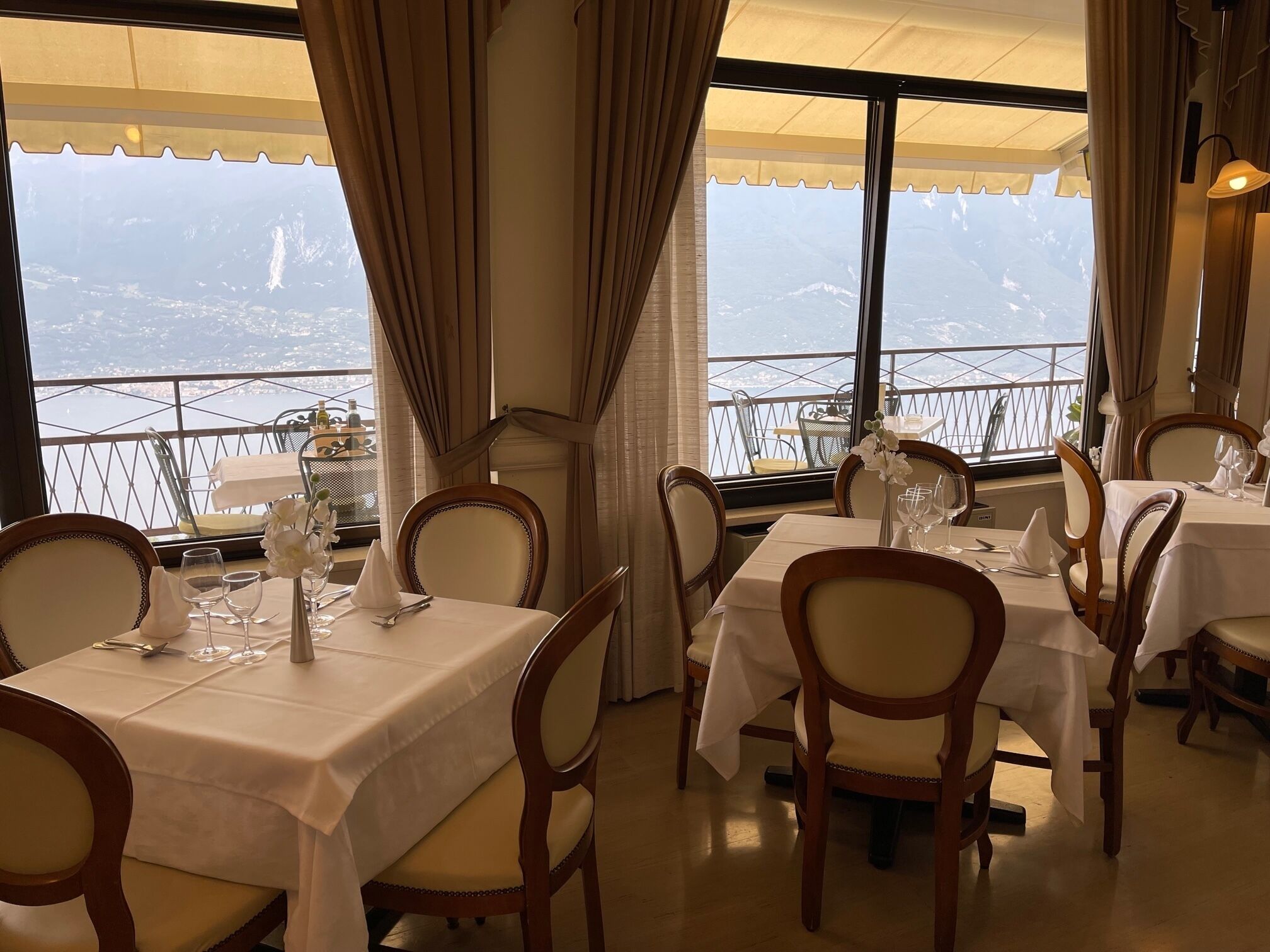 A restaurant with tables set for dining, chairs, and a view of the cityscape through large windows.