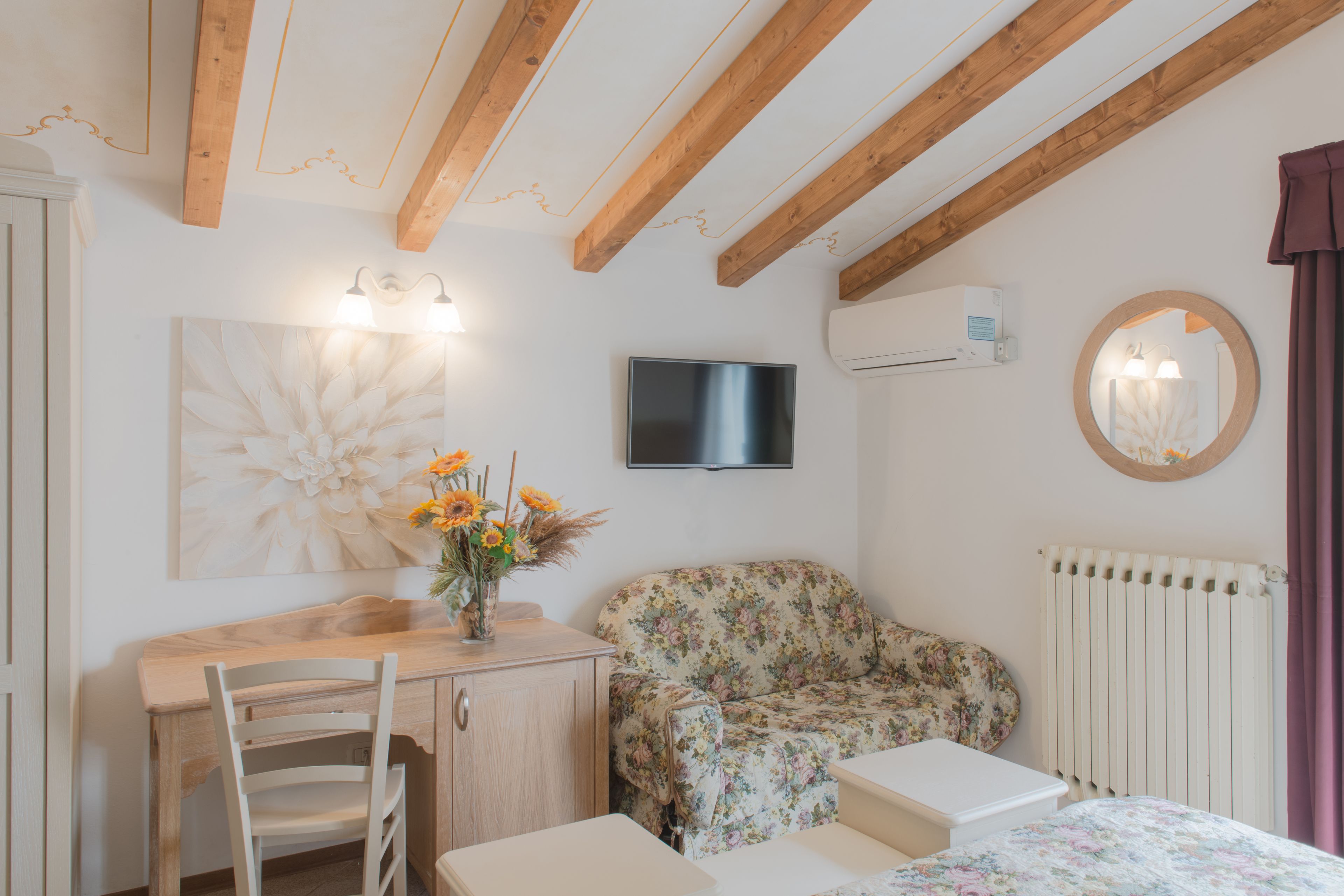 A room with a wooden ceiling, a flat-screen TV, a floral sofa, a small table, and a chair.