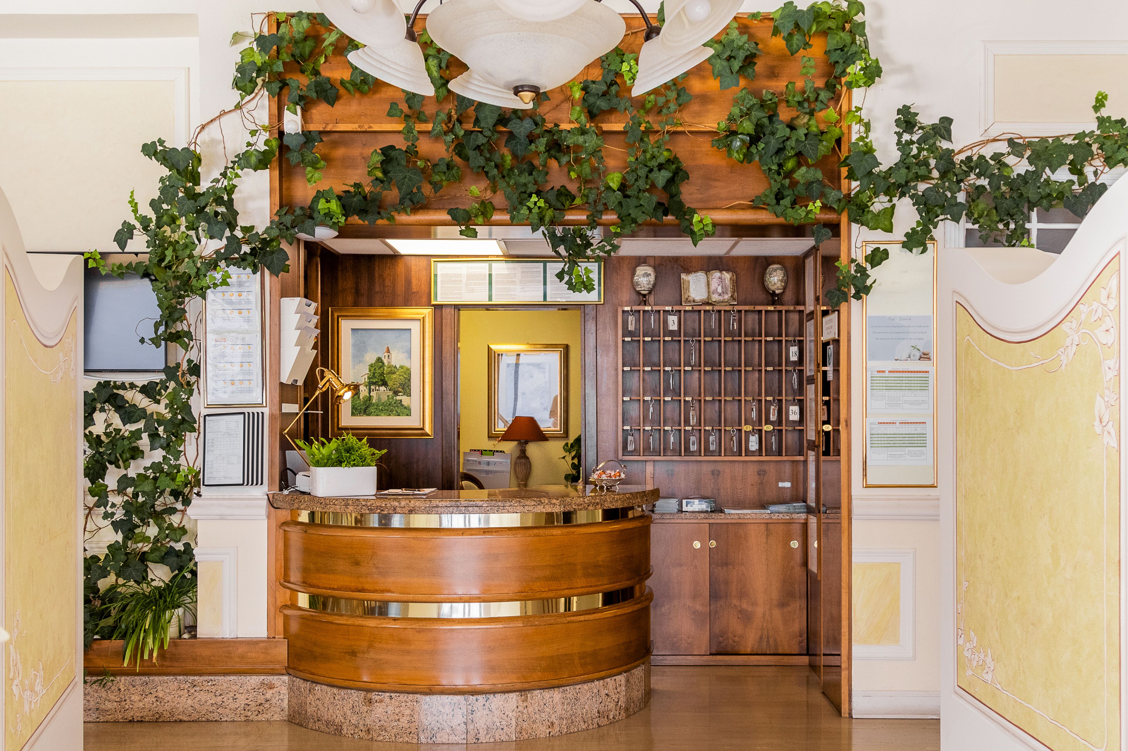 A reception area with a wooden reception desk, framed artwork, a plant, and a wall-mounted display.