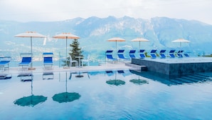 Una piscina con agua azul cristalina, rodeada de sillas de descanso y sombrillas azules, con una montaña al fondo.