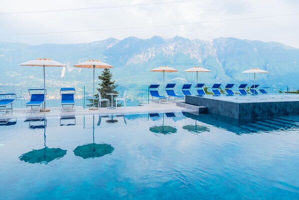 Ein Pool mit klarem, blauem Wasser, umgeben von blauen Liegestühlen und Sonnenschirmen, mit Blick auf einen Berg.
