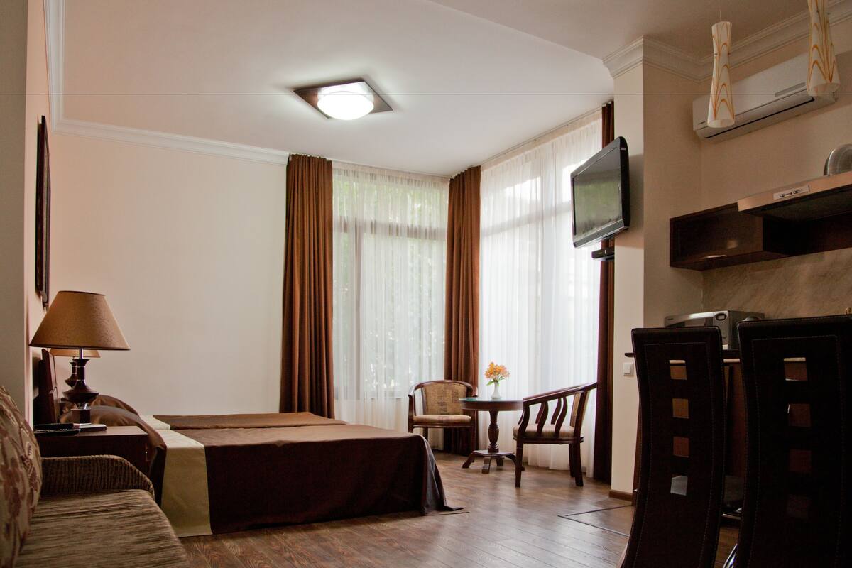 A hotel room with a bed, a desk with a lamp, a chair, a television, and a window with curtains.