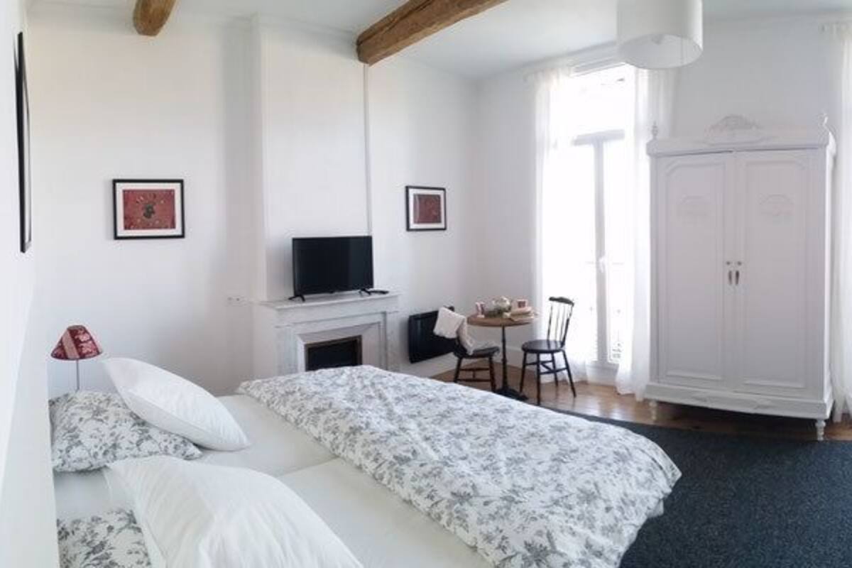 A bedroom with a bed, a sofa, a small table, a TV, a wardrobe, and a fireplace.