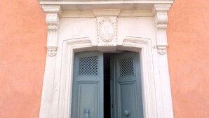 Una entrada de edificio con dos puertas, un balcón decorativo y una fachada sencilla y sin adornos.