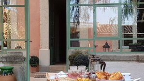 Un área de comedor al aire libre con una mesa preparada para el desayuno, incluyendo pan, bollería y bebidas.