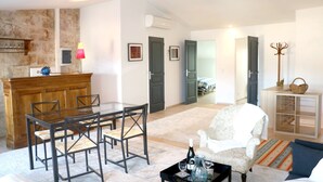 Un salón con una mesa de comedor de madera y sillas, un sillón blanco, una mesa de centro y una estantería.