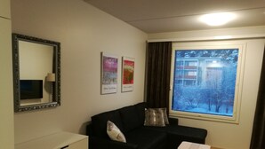 Een knus leefruimte met een zwarte bank, een klein wit tafeltje, een spiegel en een raam met uitzicht op een besneeerd landschap.