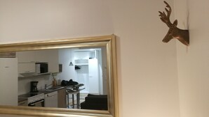 Een keuken met witte kasten, een fornuis en een magnetron. Een spiegel met gouden lijst hangt aan de muur en weerspiegelt de keuken.