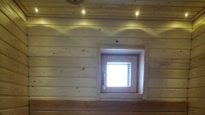 Een sauna met houten banken, een klein raam en een emmer met een handdoek.
