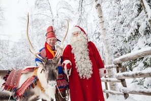 A reindeer and a person in a red outfit with antlers, standing in a snowy forest. - Rovavisit Apartments (Rovaniemi)