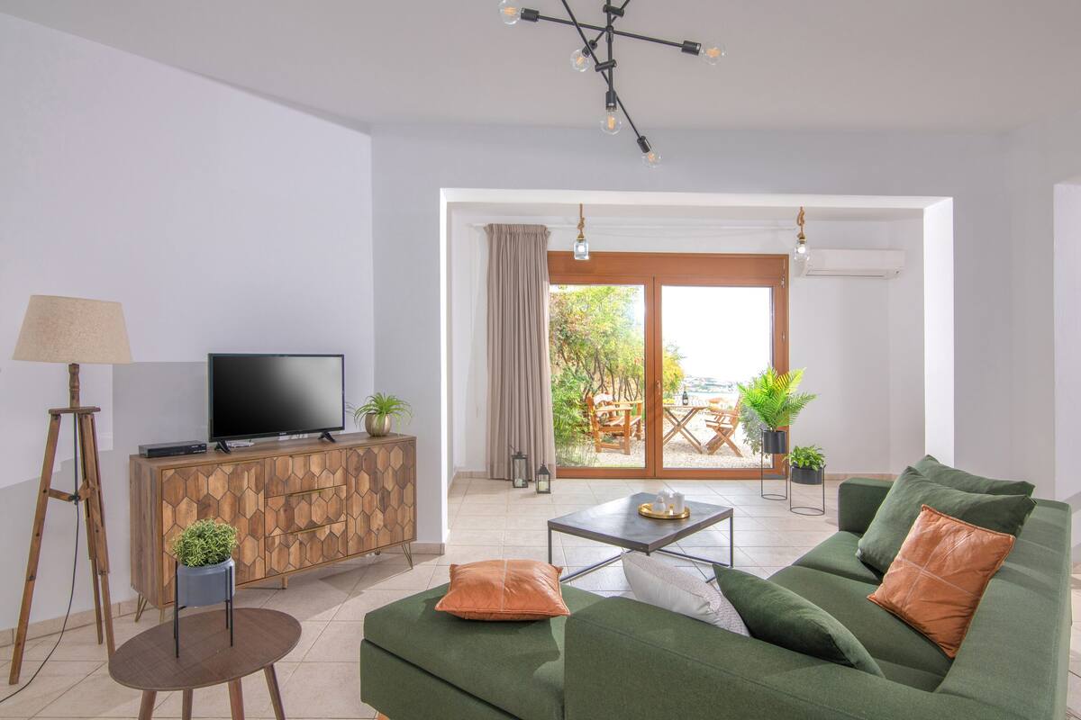 A modern living room with a green sofa, a wooden cabinet, a television, and a small table.