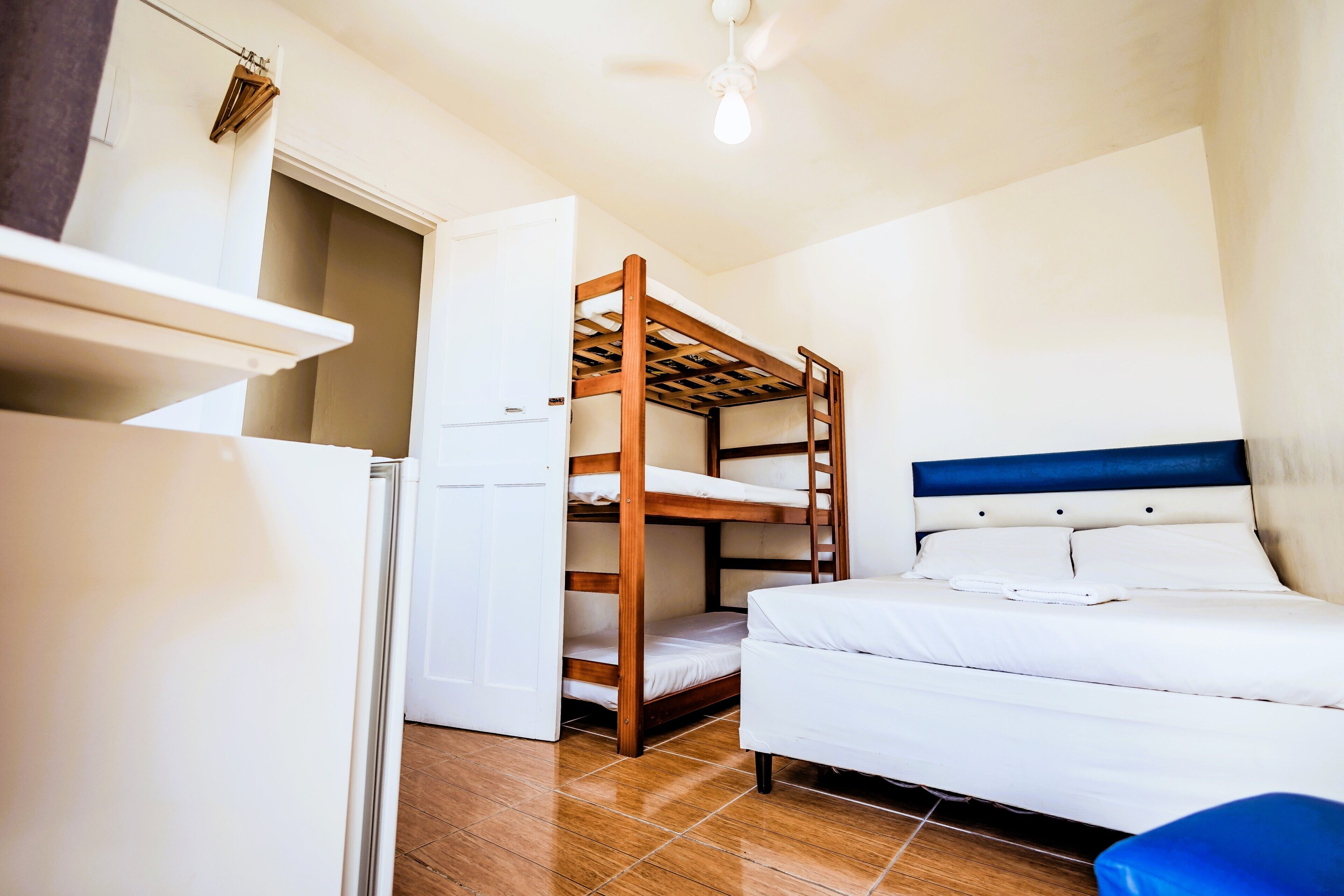 A compact room with a bunk bed, a single bed, a small refrigerator, and a ceiling fan.