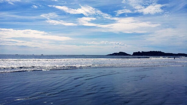 Une plage avec un ciel dégagé, une mer calme et des reliefs visibles au loin.