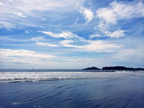 Una playa con cielo despejado, mar tranquilo y formaciones terrestres a lo lejos.