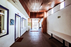 A corridor with a wooden ceiling, tiled floor, and a bench on the right. - Pousada Peruibe 455 (Peruíbe)