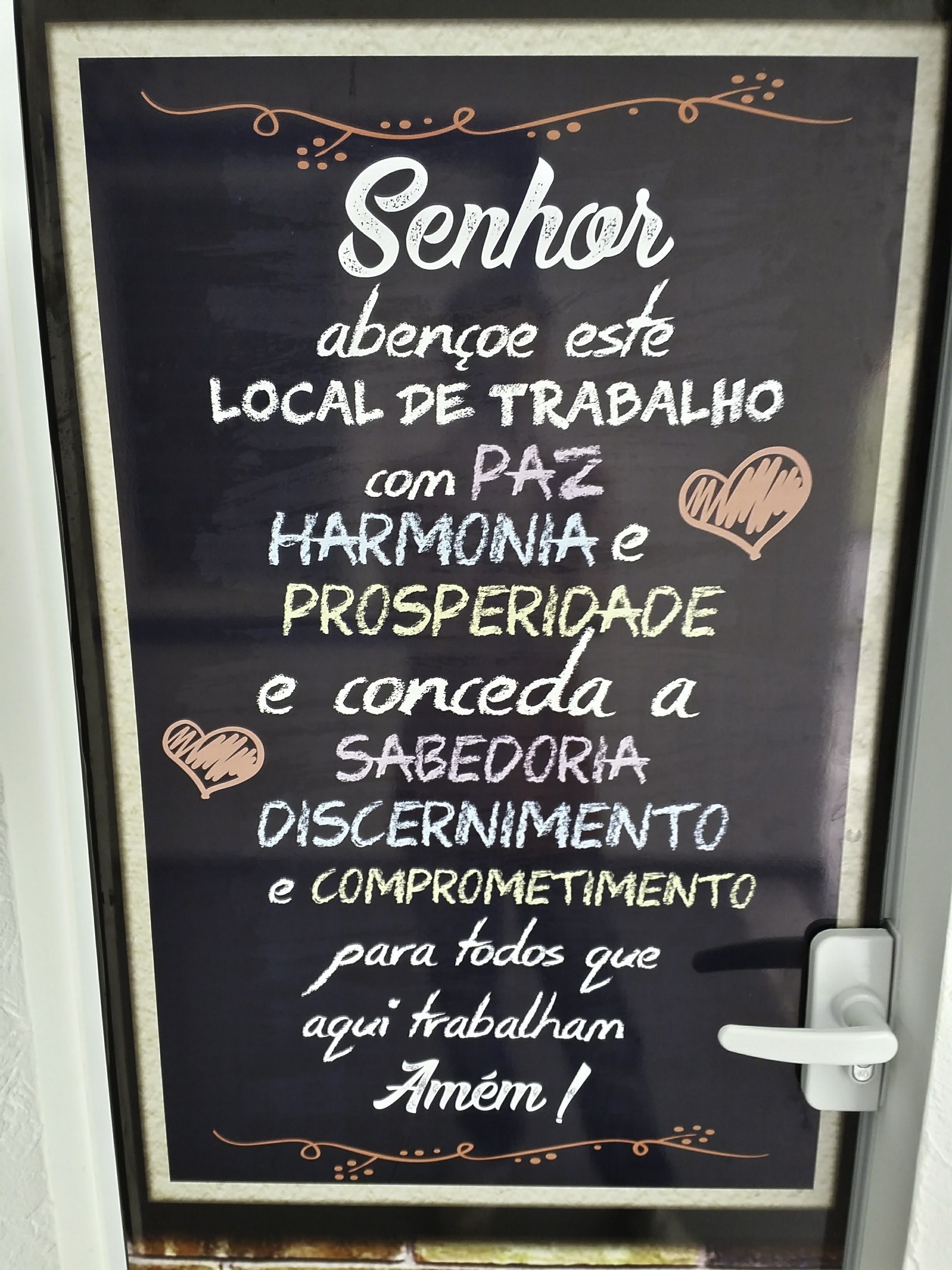 Una pissarra amb un missatge en portuguès, emmarcada i penjada en una porta.