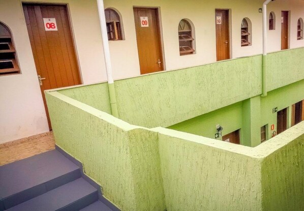 Un edificio con varias habitaciones, cada una con una puerta numerada. Hay escalones que llevan a una zona pintada de verde con barandilla.