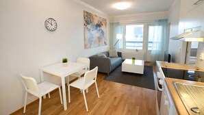 A modern living room with a dining area, a gray sofa, a white coffee table, and a kitchen area with a stove. - RovaVisit Center (Rovaniemi)