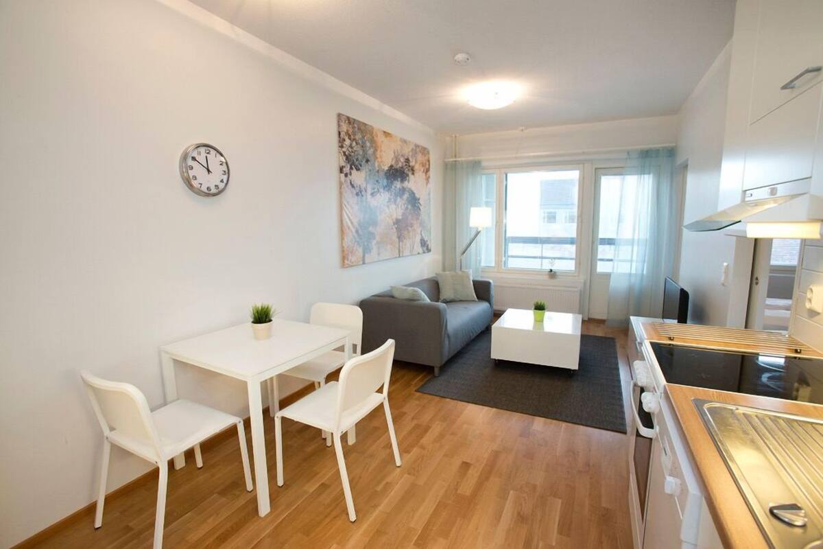 A modern living room with a dining area, a gray sofa, a white coffee table, and a kitchen area with a stove.