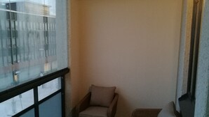 A balcony with wicker furniture, a cushioned sofa, and a view of buildings through a glass partition. - RovaVisit Center (Rovaniemi)