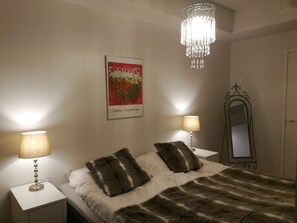 Ein Schlafzimmer mit einem Bett, zwei Nachttischlampen, einer Kristallleuchtre, einem gerahmten Kunstwerk und einem Spiegel an der Wand.