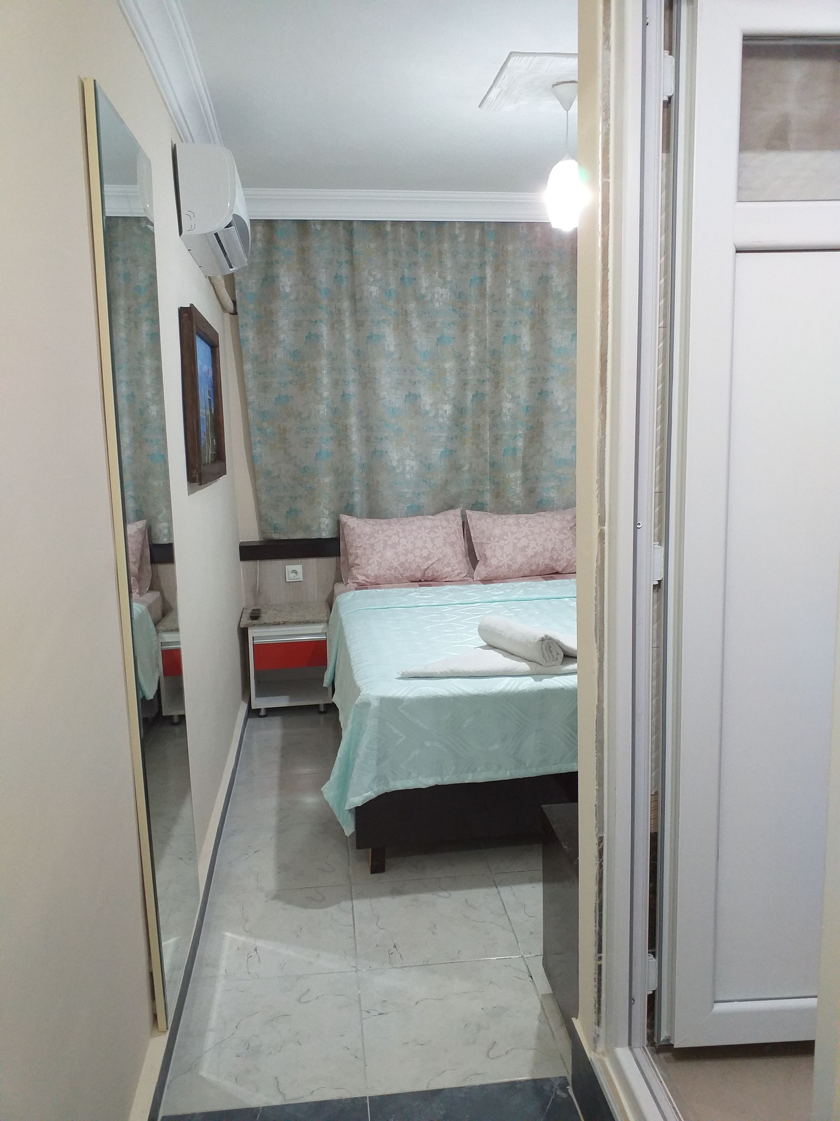 Un dormitorio con cama, mesita de noche, espejo y ventana con cortinas.