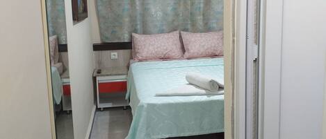 Un dormitorio con cama, mesita de noche, espejo y ventana con cortinas.