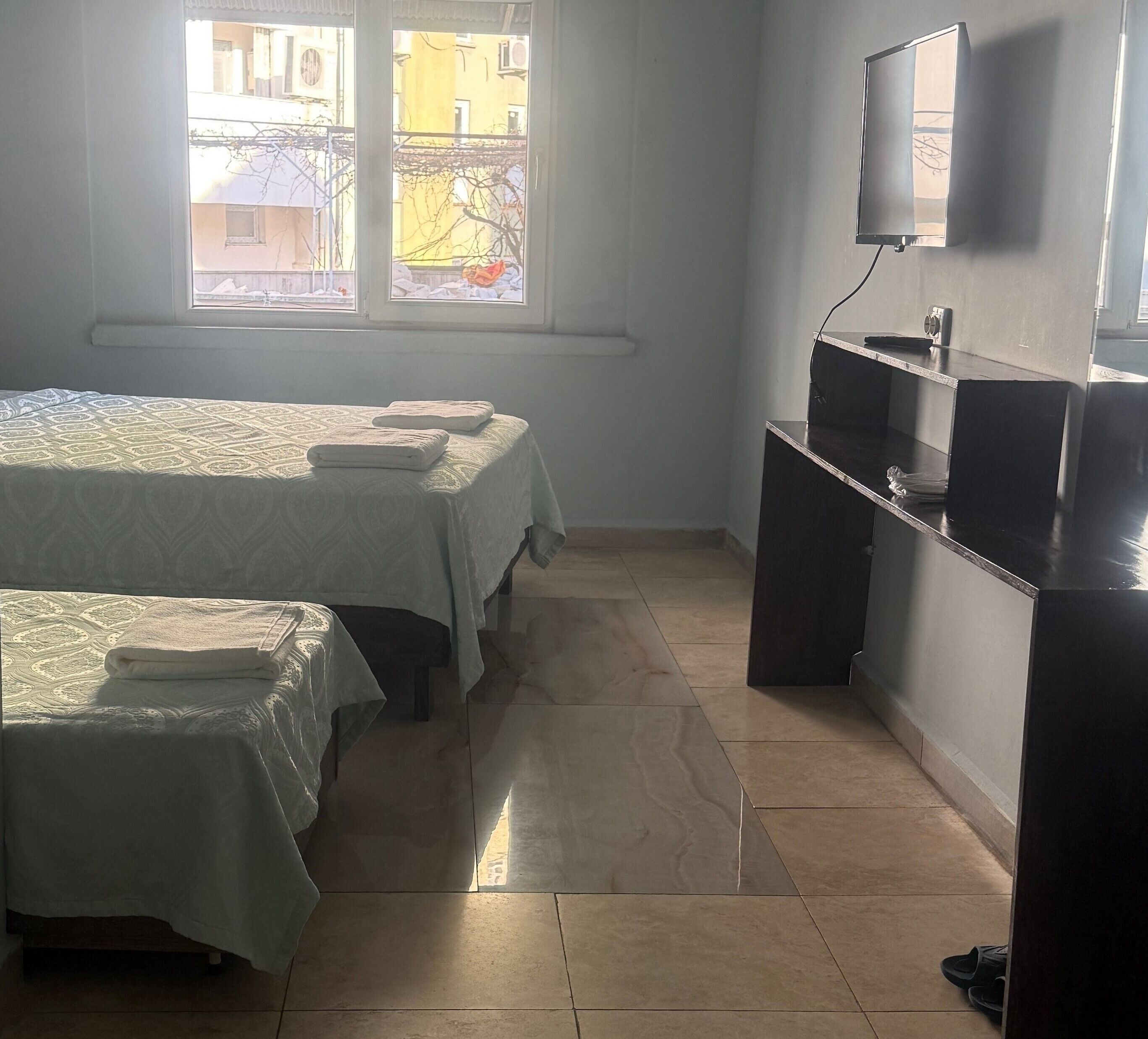 Une petite chambre propre, avec deux lits, un bureau et un téléviseur.