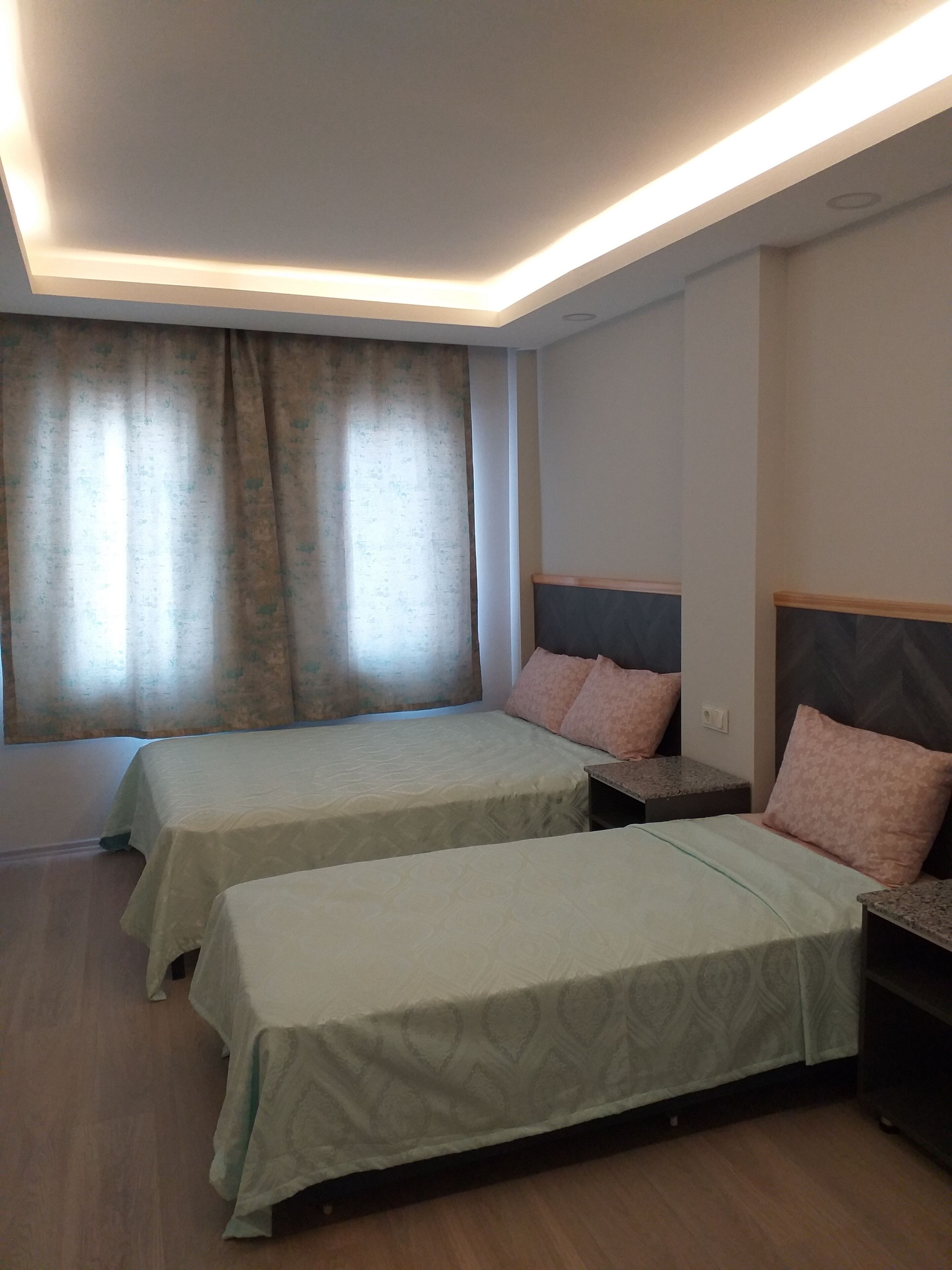 A hotel room with two beds, each with a headboard and pillows, a small table, and a window with curtains.