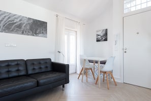 Ein modernes Wohnzimmer mit einem schwarzen Ledersofa, einem Esstisch mit Stühlen und einer weißen Tür.