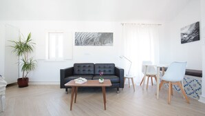 Un salon moderne avec un canapé en cuir foncé, une table basse en bois, une plante en pot et un coin repas comprenant une table et des chaises blanches.
