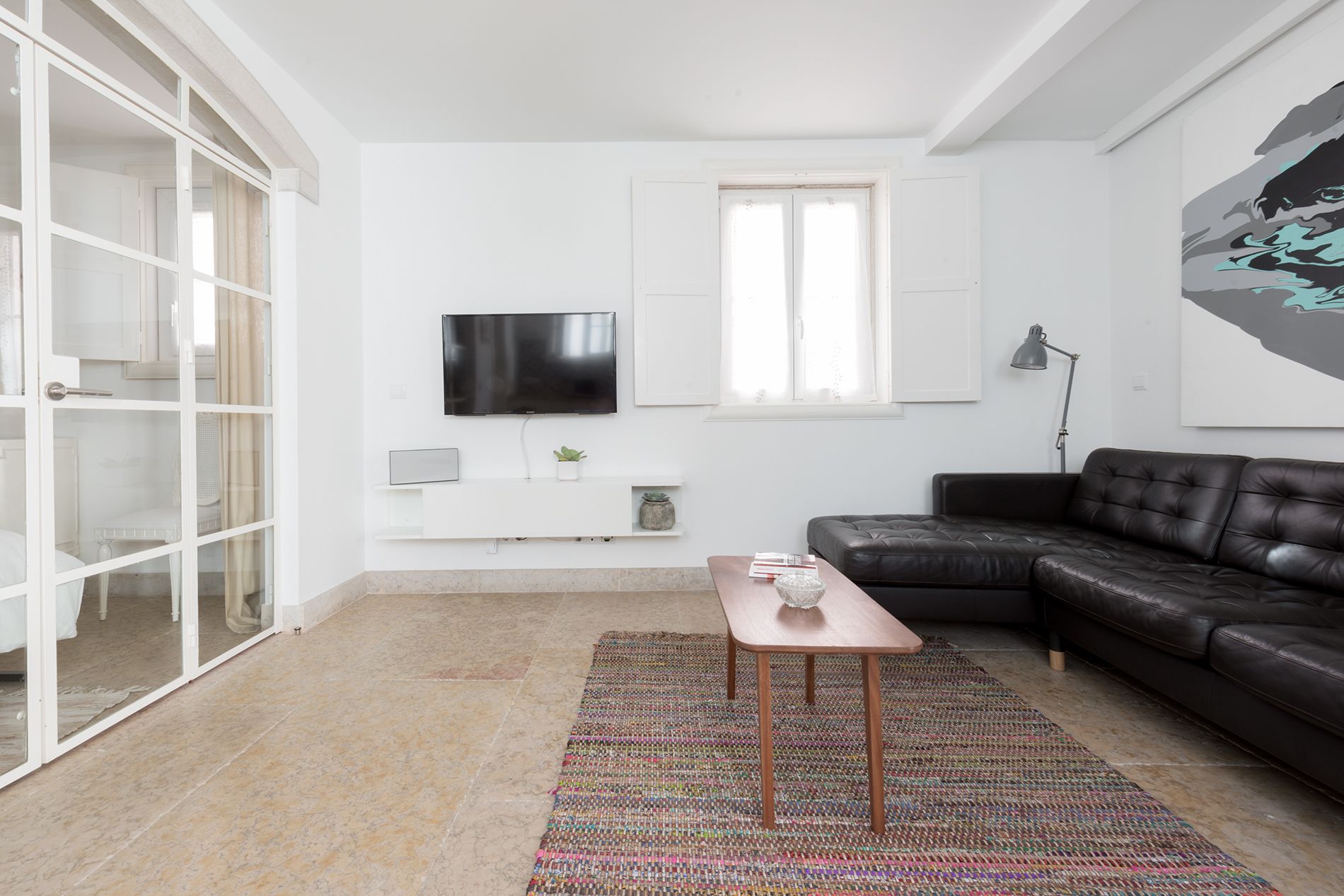 Ein modernes Wohnzimmer mit einer schwarzen Ledersofa, einem weißen Fernseher an der Wand und einem gemusterten Teppich auf dem Boden.