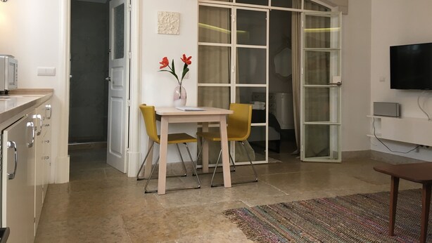 Un salon moderne comprenant un coin repas, un téléviseur fixé au mur et une grande fenêtre avec des rideaux.