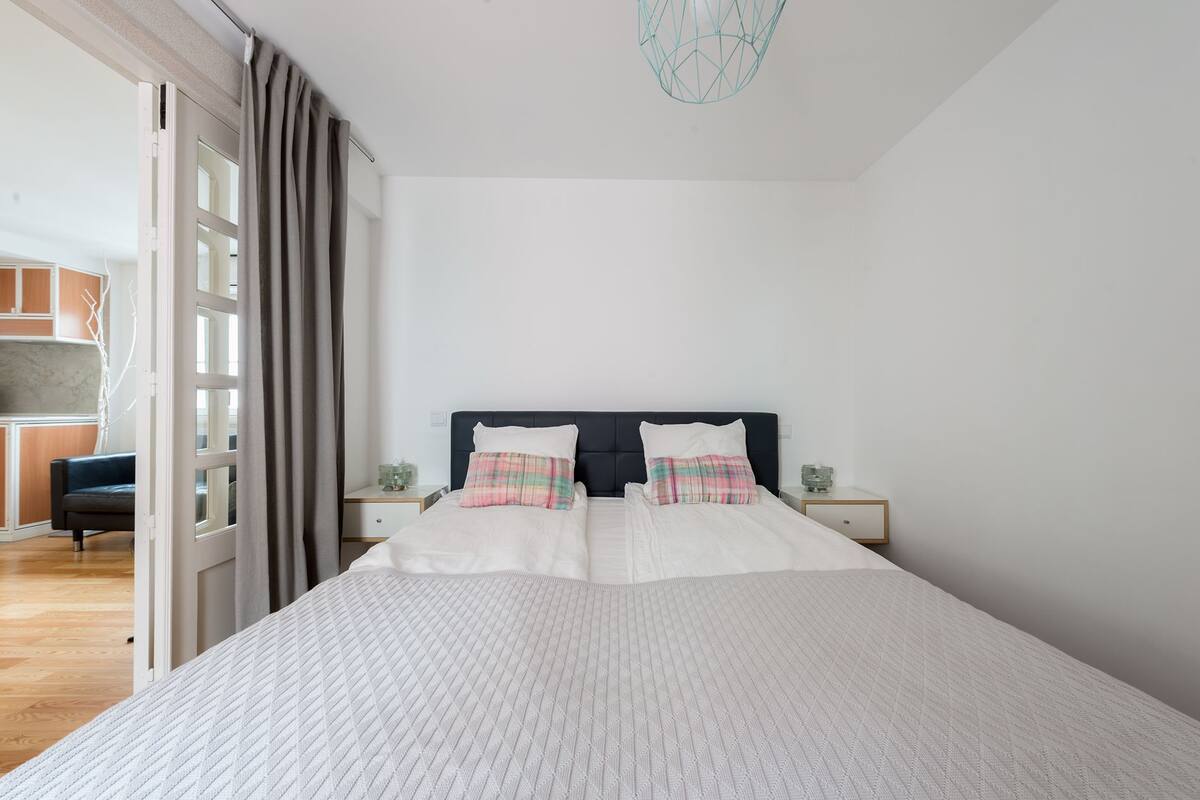 A modern bedroom with a large bed, two bedside tables, and a view of a kitchen area.