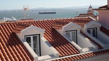 Una terraza en la azotea con tejas de terracota, dos ventanas de tejado y vistas a un barco grande en el agua.