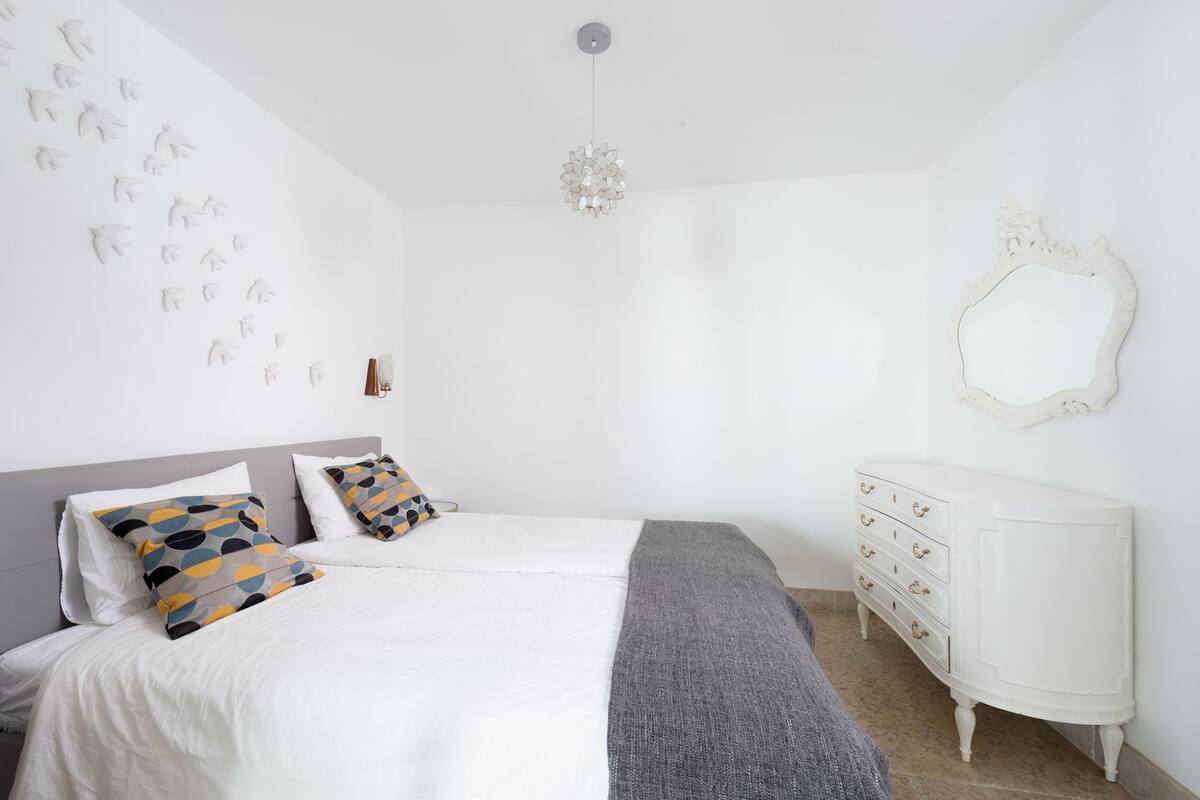 A bedroom with a bed, two pillows, a dresser, a mirror, and wall art.