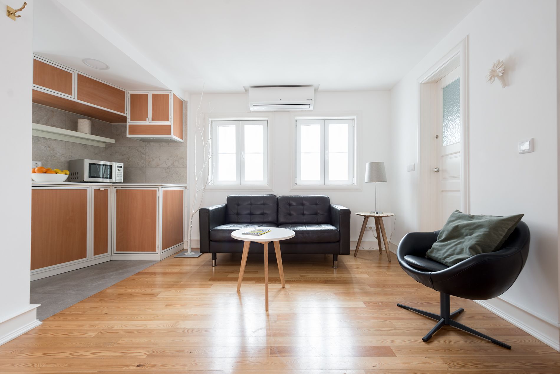 Un espacio habitable compacto con kitchenette, un sofá de cuero negro, una mesa redonda y una silla moderna.