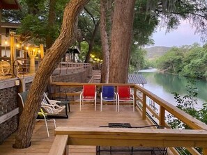 A wooden deck with chairs overlooking a river, surrounded by trees and a stone wall.