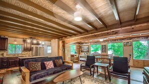 A spacious living area with a dark-colored sofa, wooden coffee table, and two chairs. A large rug covers the floor, and the room has a high ceiling with exposed wooden beams. - Ponderosa Cabin (New Braunfels)