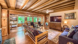 A spacious living area with wooden beams, a sofa, a couch, a TV, and a dining area with chairs and a table. - Ponderosa Cabin (New Braunfels)