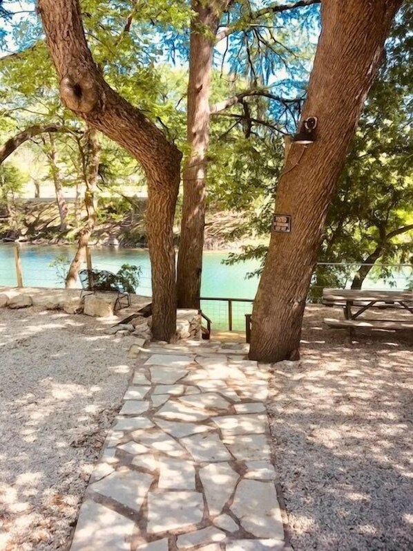 A stone pathway leading to a picnic area with benches, surrounded by trees and a body of water.