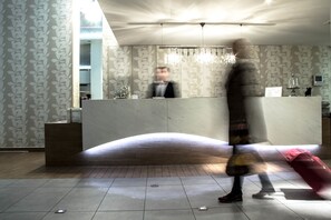 A hotel reception area with a curved reception desk, a chandelier, and patterned wallpaper. - Hotel Iliana (Ziros)