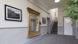 A hallway with a large ornate mirror, a framed black and white photo, and a staircase leading to an upper floor. - Owl, Hambleton by Marston's Inns (Selby)
