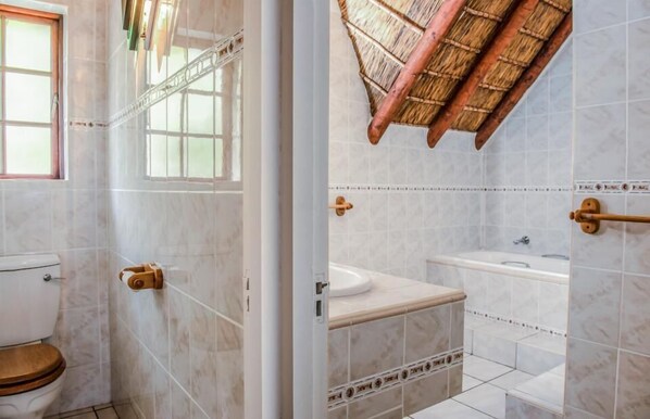 Baño con inodoro, lavamanos y zona de ducha, con azulejos blancos y pomo de madera.