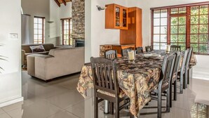 A spacious living area with a sofa, a dining table set with chairs, and a kitchen area with wooden cabinets and a large window. - St Francis Bay Luxury Lodge 2 (Saint Francis Bay)